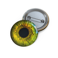 Glossy round pinback button with vivid green-yellow eye design, intense gaze, and metallic backing.