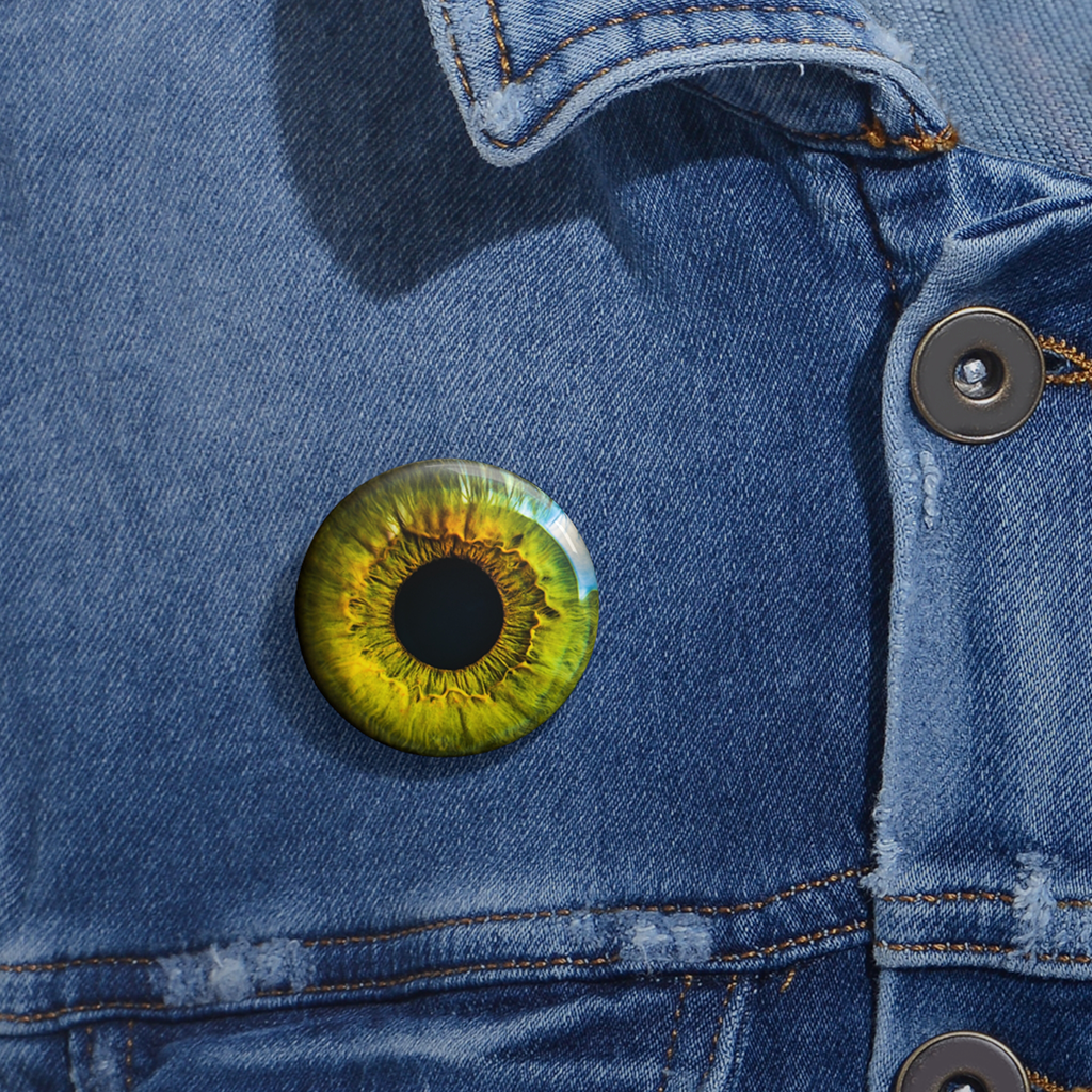 Close-up of a denim jacket with a glossy round pinback button with vivid green-yellow eye design.