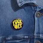Neon yellow and pink “F*ck Off” pin with a twisted smiley face and black background, glossy finish and sharp edge on a denim jacket.
