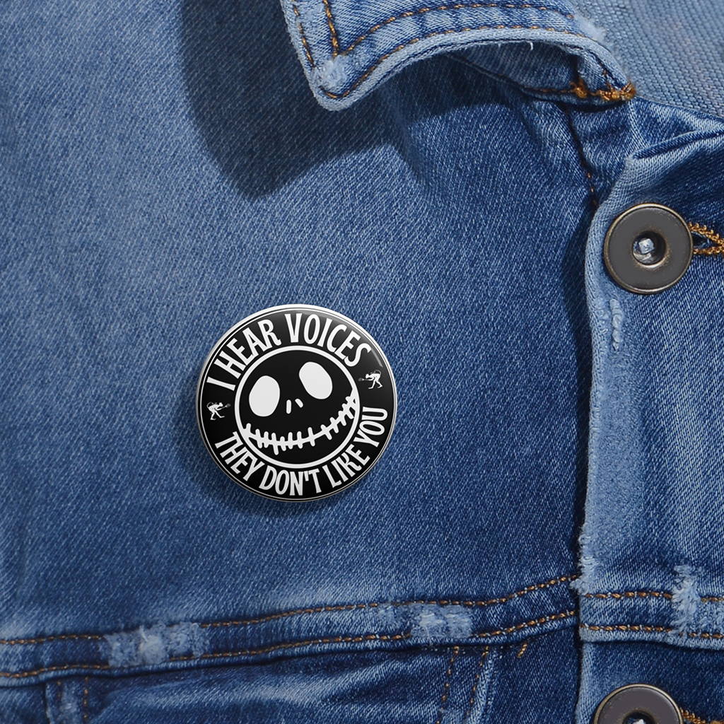 Black and white button with creepy smiley face and text “I Hear Voices, They Don’t Like You.” Glossy finish, metal backing on a denim jacket.